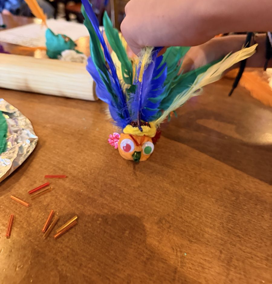 A playdough creature with googly eyes and blue, green and yellow feathers